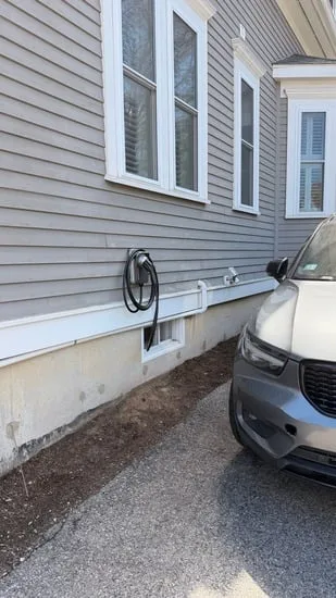 Exterior view of a residential EV charger installation mounted on house siding next to a parked car.